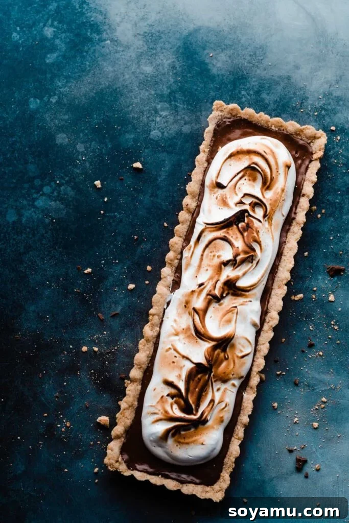Gourmet S'mores Tart with Torched Meringue 2 A beautifully crafted S'mores Tart resting on a vibrant blue surface, showcasing its perfectly toasted marshmallow meringue.