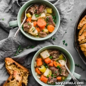 A bowl of Irish stew with fresh herbs on top, accompanied by a side of bread.