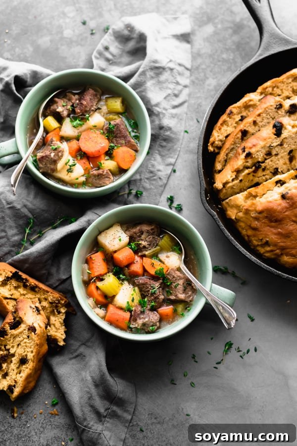 Two bowls of Irish stew with a large loaf of Irish soda bread in the background.