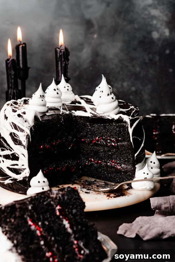 A beautifully sliced Black Velvet Cake, showcasing its deep black layers, vibrant raspberry filling, and silky frosting, whimsically topped with meringue ghosts and delicate marshmallow spiderwebs. The perfect Halloween or party centerpiece.