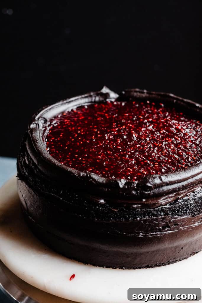 A three-tiered Black Velvet Cake in the process of being assembled, vividly showcasing its distinct dark chocolate layers, the generous amount of rich frosting, and the bright, luscious raspberry filling visible between the tiers.