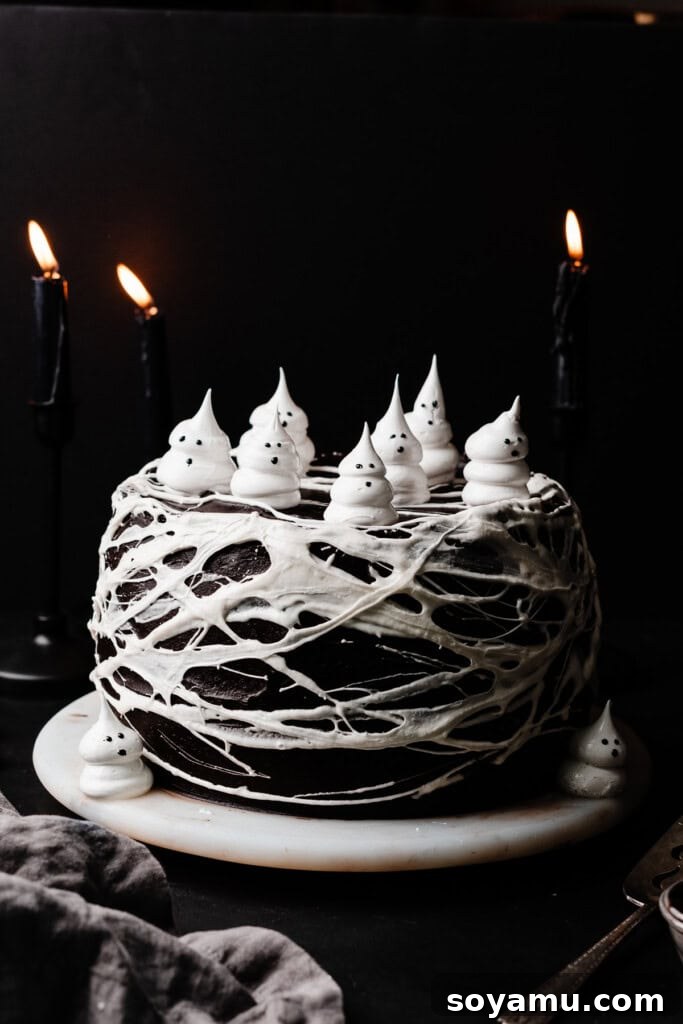 A fully assembled and exquisitely decorated Halloween-themed Black Velvet Cake, adorned with charming meringue ghosts and delicate marshmallow spiderwebs, beautifully presented on an elegant marble cake plate, ready for a spooky celebration.