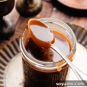 A spoonful of butterscotch sauce balancing on a jar of the sauce.