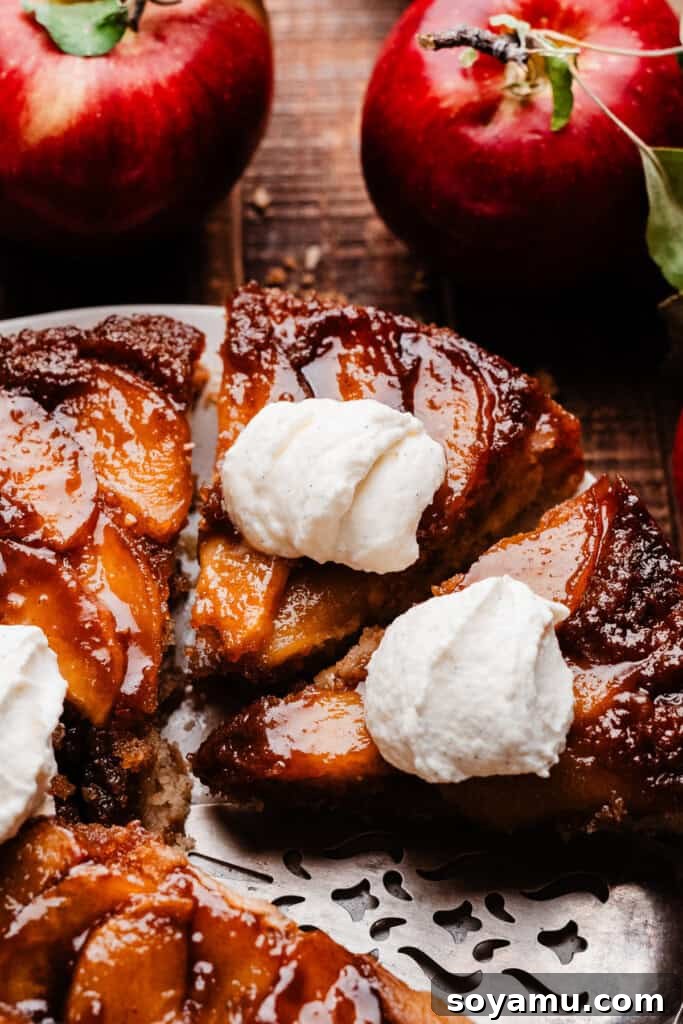 Sticky Apple Caramel Cake 2 A beautifully sliced apple upside down cake on a cake plate, adorned with a dollop of whipped cream, showcasing the rich caramel and tender apple layers.