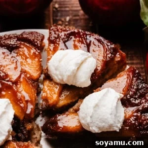 A close-up on the sliced apple upside down cake, with dollops of whipped cream on top.
