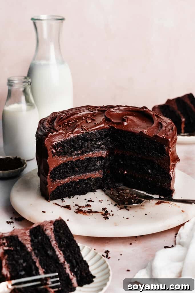 Ultimate Eggless Chocolate Fudge Cake 2 A beautifully sliced eggless chocolate cake on a marble cake plate, with individual slices and glasses of milk arranged nearby, inviting indulgence.