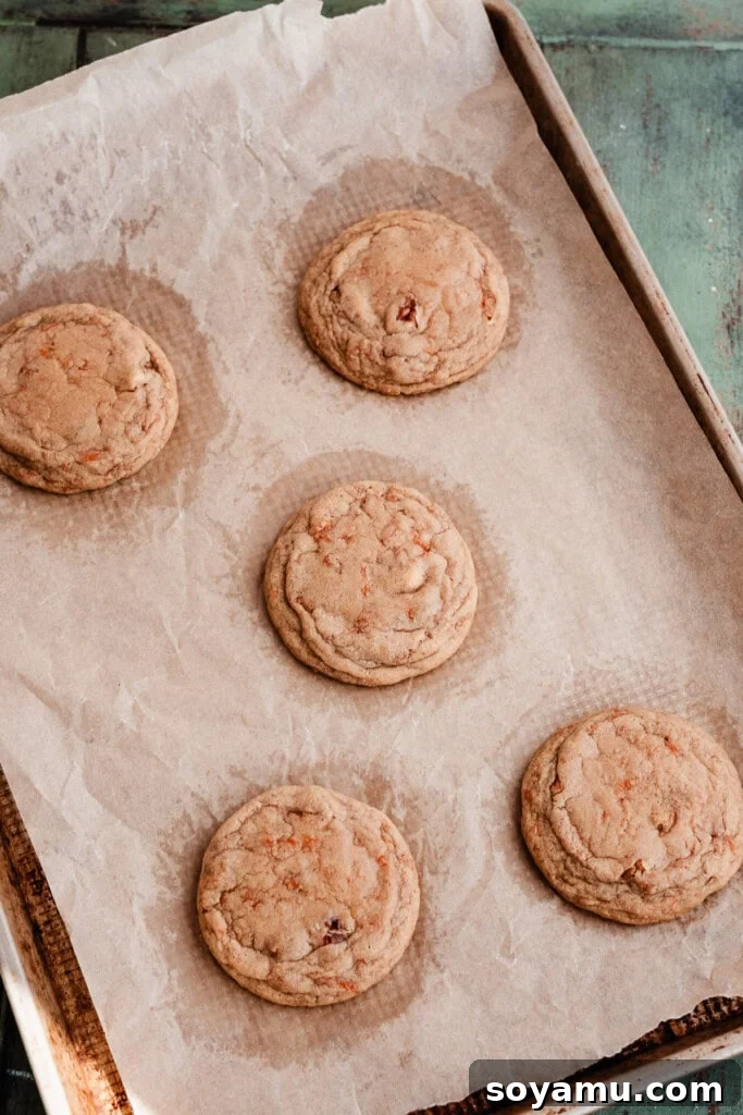 Spiced Carrot Cake Cookies with Brown Butter Cream Cheese 7 Freshly baked carrot cake cookies cooling on a cookie sheet, their golden edges visible.