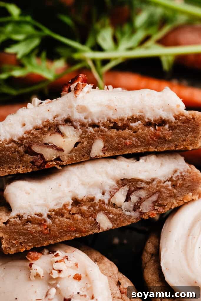 Spiced Carrot Cake Cookies with Brown Butter Cream Cheese 9 A close-up image of a carrot cake cookie broken in half, revealing its moist, chewy interior filled with carrot flecks and pecans, and a generous layer of frosting.