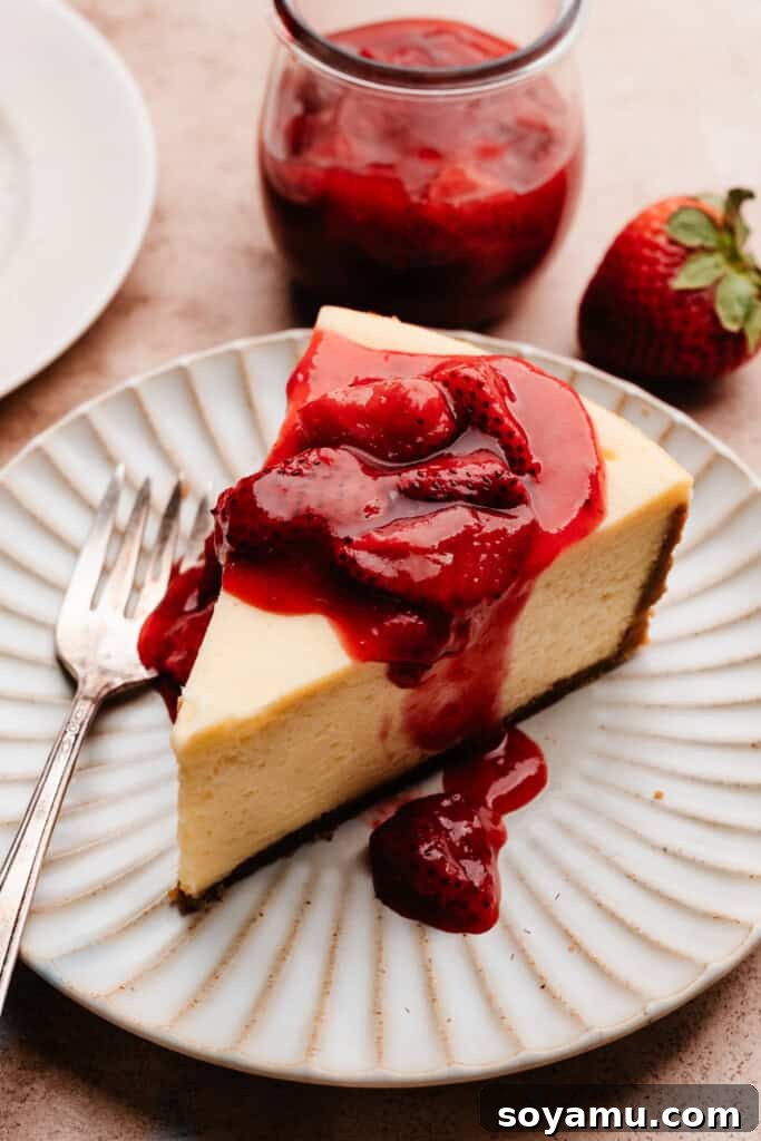 Velvety Rich New York Cheesecake Masterpiece 13 A slice of creamy New York Style Cheesecake beautifully adorned with a vibrant strawberry sauce, ready to be enjoyed.