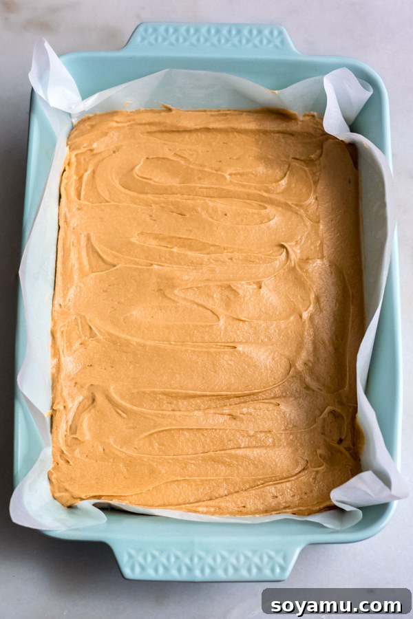 Blondie Batter Ready for Baking: Achieving Even Texture Smooth blondie batter spread evenly into a parchment-lined baking pan, ready for the oven.