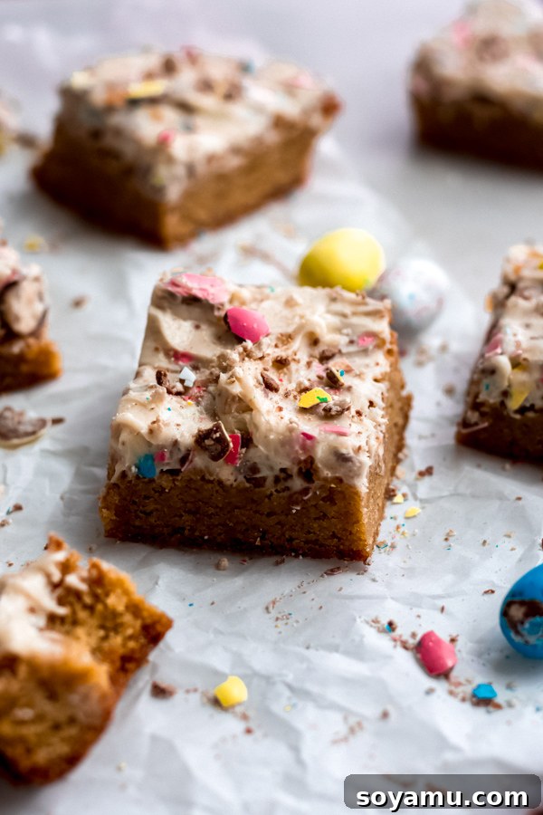 Beautifully Decorated Easter Egg Blondies with Festive Candy Topping A close-up of a tray of fully frosted Easter egg blondies, topped with colorful whole and crushed Robin Egg candies, ready to be cut.
