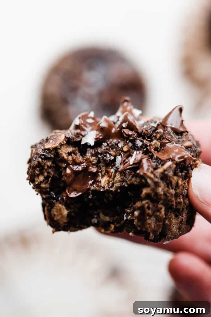Wholesome Banana Chocolate Oat Muffins 3 A close-up view of a freshly baked banana chocolate oat muffin with a bite taken out, revealing gooey melted chocolate chips and a moist interior.