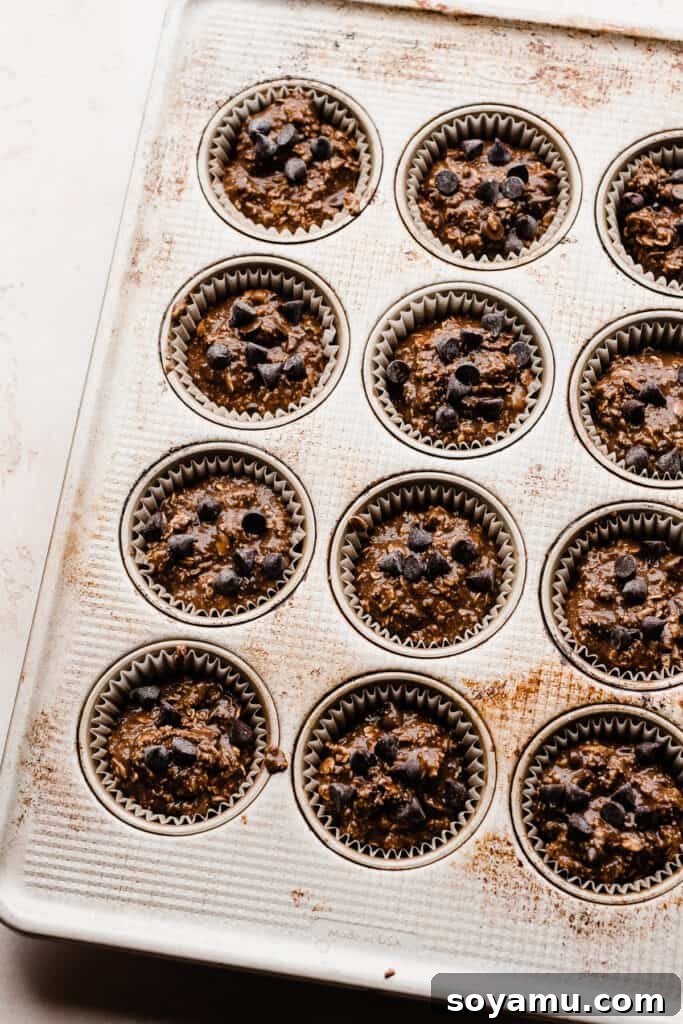 Wholesome Banana Chocolate Oat Muffins 6 A muffin tin with paper liners, filled with the raw banana chocolate oat muffin batter, topped with extra chocolate chips.