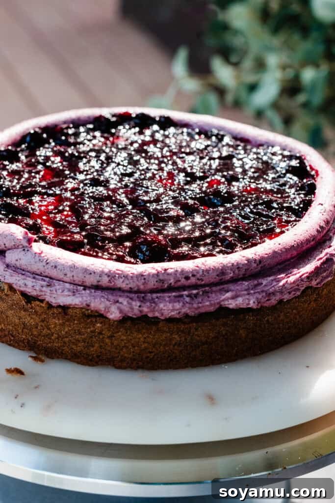 Blueberry Bliss Cake 15 The first cake layer topped with a smooth layer of frosting, a piped frosting border, and a generous amount of blueberry filling contained within the border.