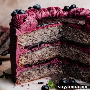 The sliced blueberry cake on a cake plate, with stunning layers of blueberry cake, blueberry filling, and blueberry frosting.