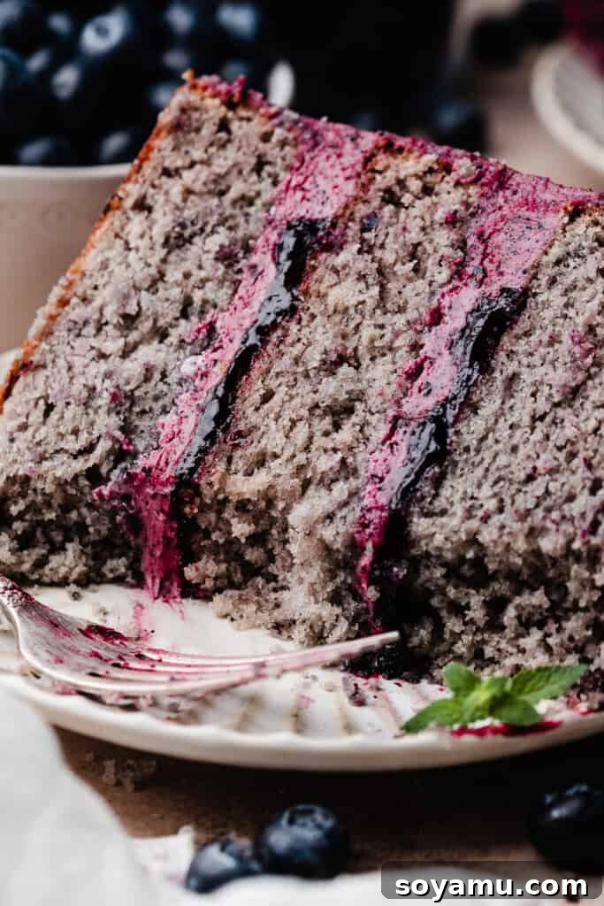 Blueberry Bliss Cake 3 A close-up view of a slice of blueberry cake on a white plate, with a few bites taken, revealing the moist cake layers and generous blueberry filling.