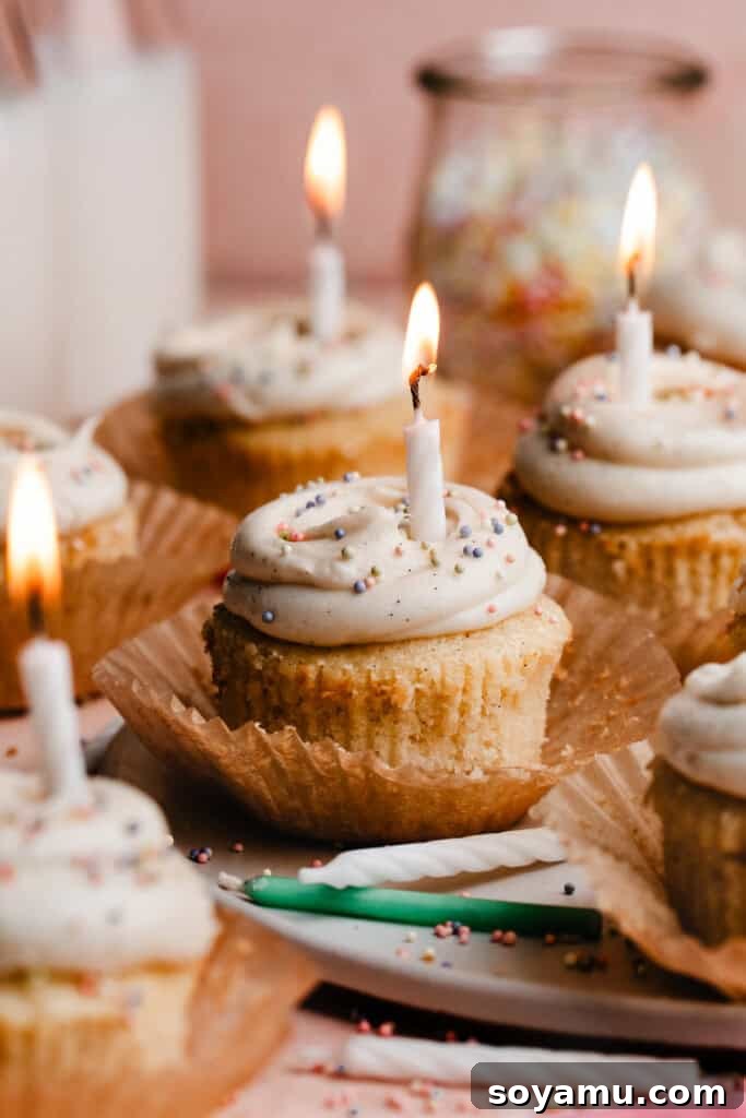 A stunning display of vanilla cupcakes, frosted and adorned with sprinkles, with flickering birthday candles on a beautiful cake plate, ready for celebration.
