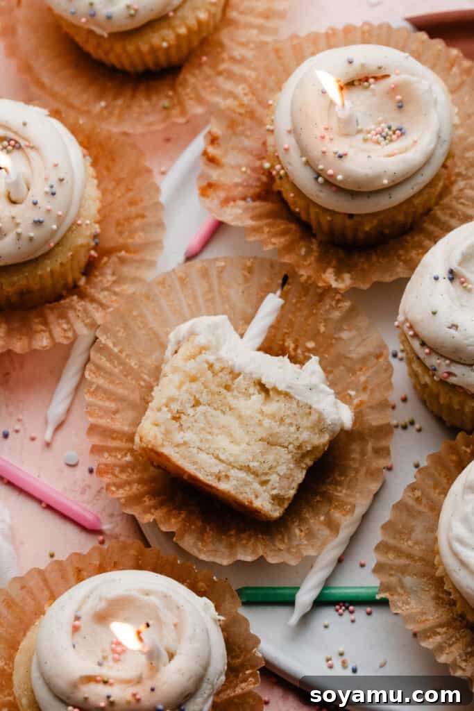 A perfectly baked, fluffy vanilla cupcake, cut in half to showcase its exquisite texture, resting alongside other frosted cupcakes on a cake plate.