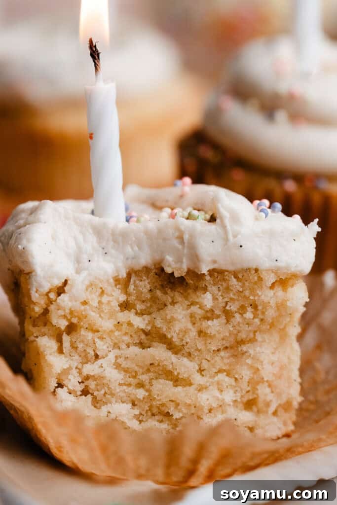 A close-up shot of a vanilla cupcake with a piece bitten off, highlighting its incredibly fluffy and moist interior texture.