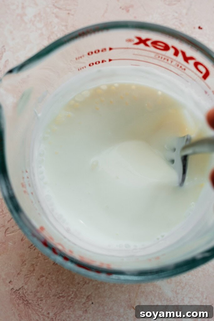 A measuring cup containing a whisked mixture of sour cream, milk, water, and vinegar, ready to be added to the cupcake batter.
