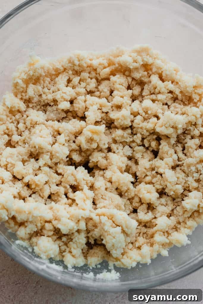 A bowl containing the flour and butter mixture, now more cohesively mixed but still notably lumpy, after the initial addition of wet ingredients.