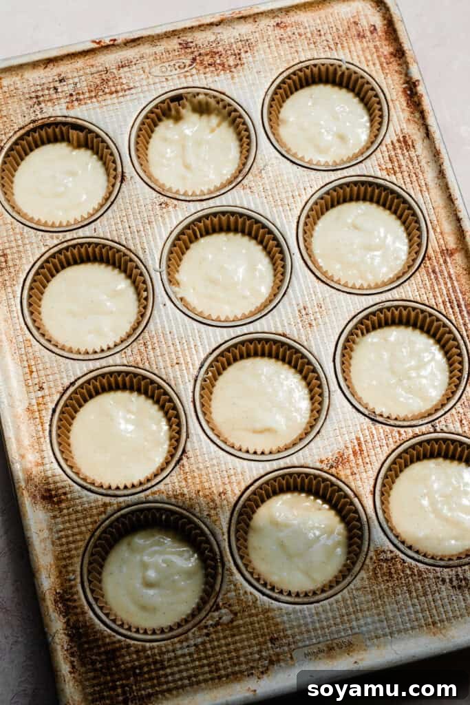 A cupcake pan, neatly lined with cupcake papers and evenly filled with vanilla cupcake batter, ready to be baked.