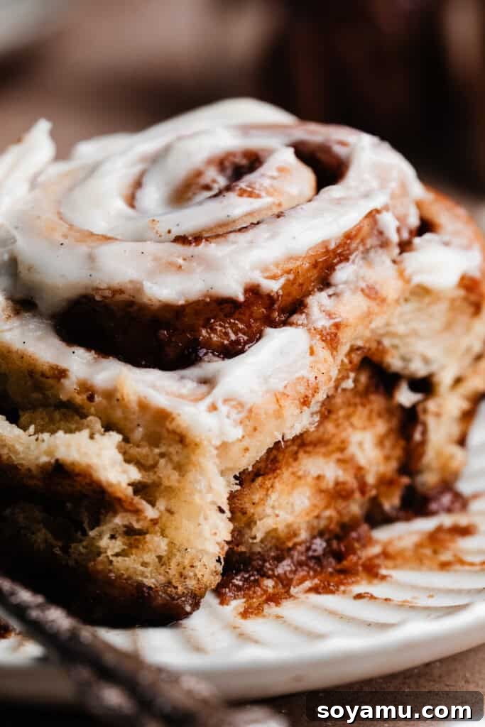 A close-up of a single gooey cinnamon roll on a plate, adorned with frosting and showcasing the rich caramel sauce at its base.