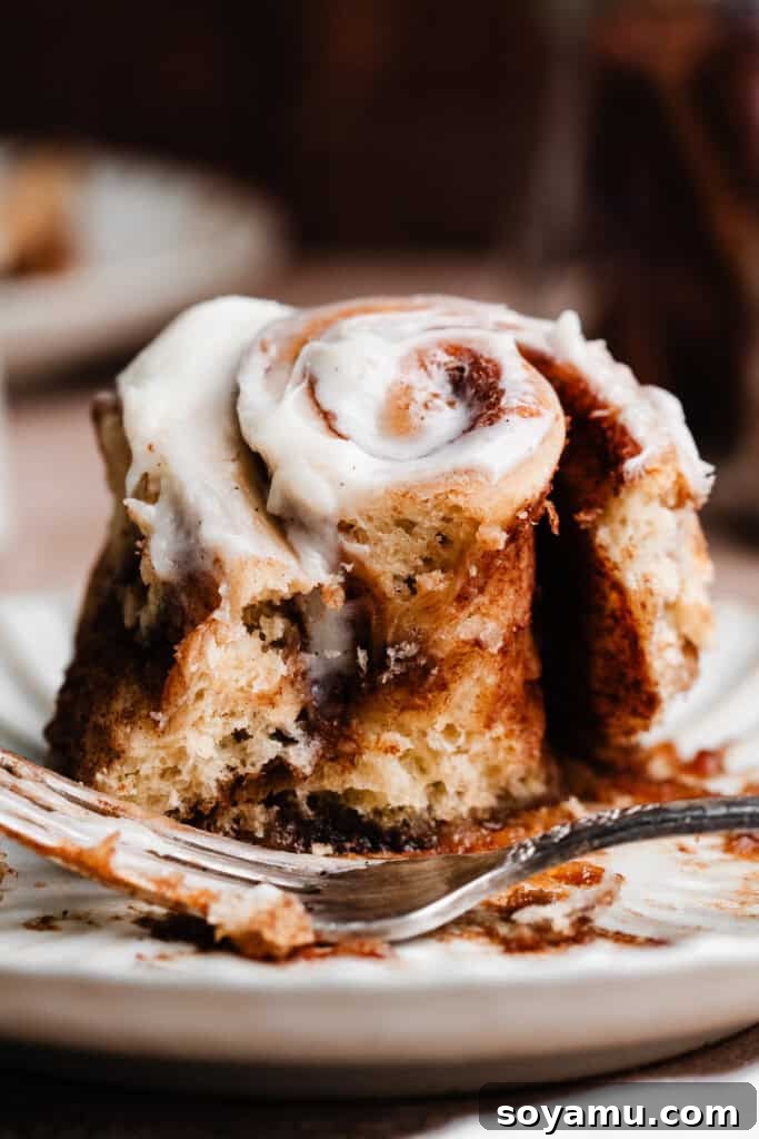 A cinnamon roll on a plate with a bite taken out, revealing the soft, layered dough inside.