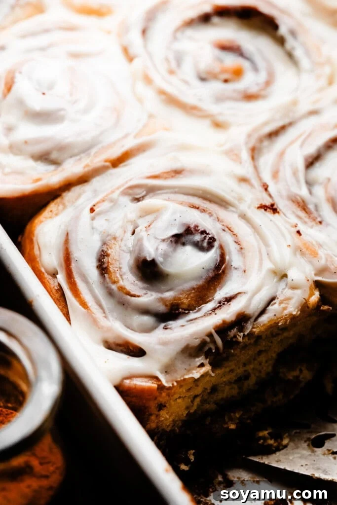 A close-up of a single, frosted cinnamon roll resting in the baking pan, showing its perfect spiral and gooey texture.