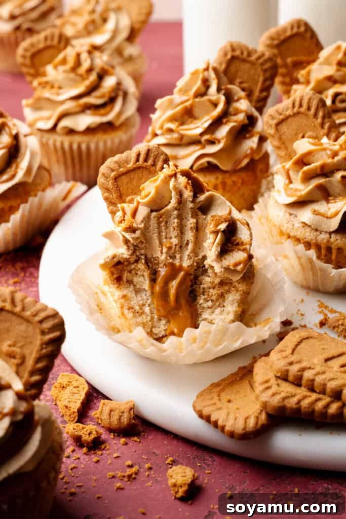 Biscoff Overload Cupcakes 14 Biscoff cupcakes on a marble cake plate, with one cupcake missing a few bites, revealing the filling inside.