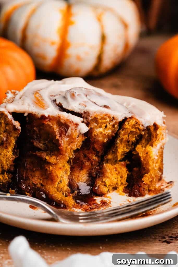 A pumpkin cinnamon roll served on a white plate, with a bite removed to show its soft texture.