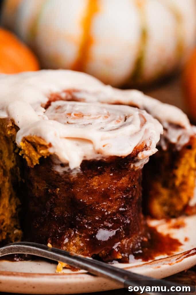 A close-up of a pumpkin cinnamon roll with a bite taken, revealing its soft, gooey interior and multiple layers of filling.