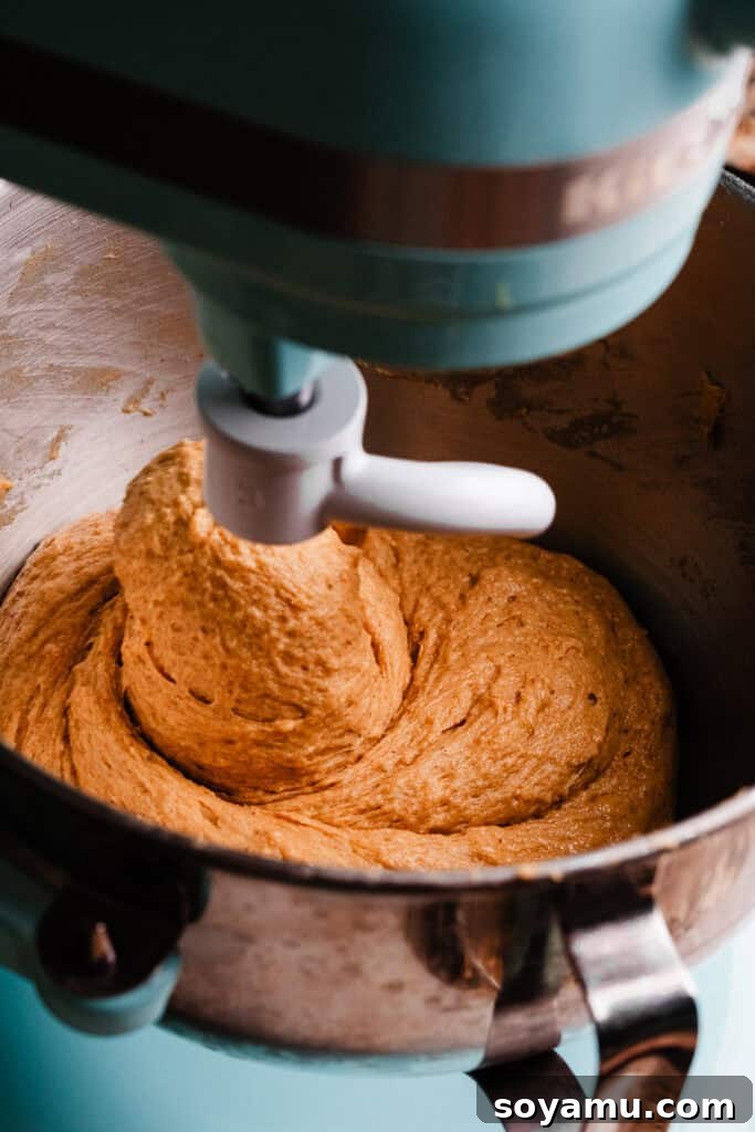The dough hook attachment kneading the pumpkin cinnamon roll dough in a stand mixer.