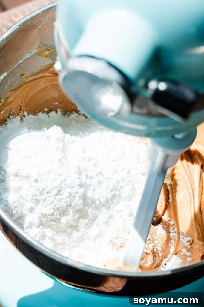 Decadent Peanut Butter Frosting Ready in 10 7 Powdered sugar being carefully added to the peanut butter and butter mixture in the mixing bowl.
