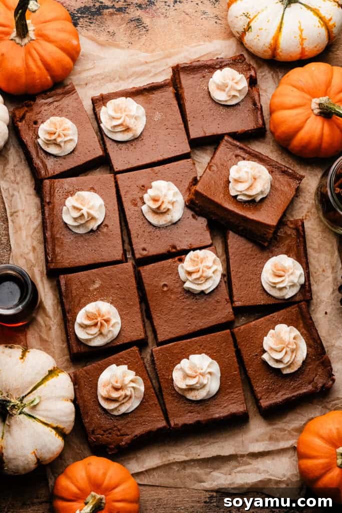 Perfectly Simple Pumpkin Pie Bars 3 The sliced pumpkin pie bars on a rustic wooden surface, each adorned with a piped swirl of whipped cream.