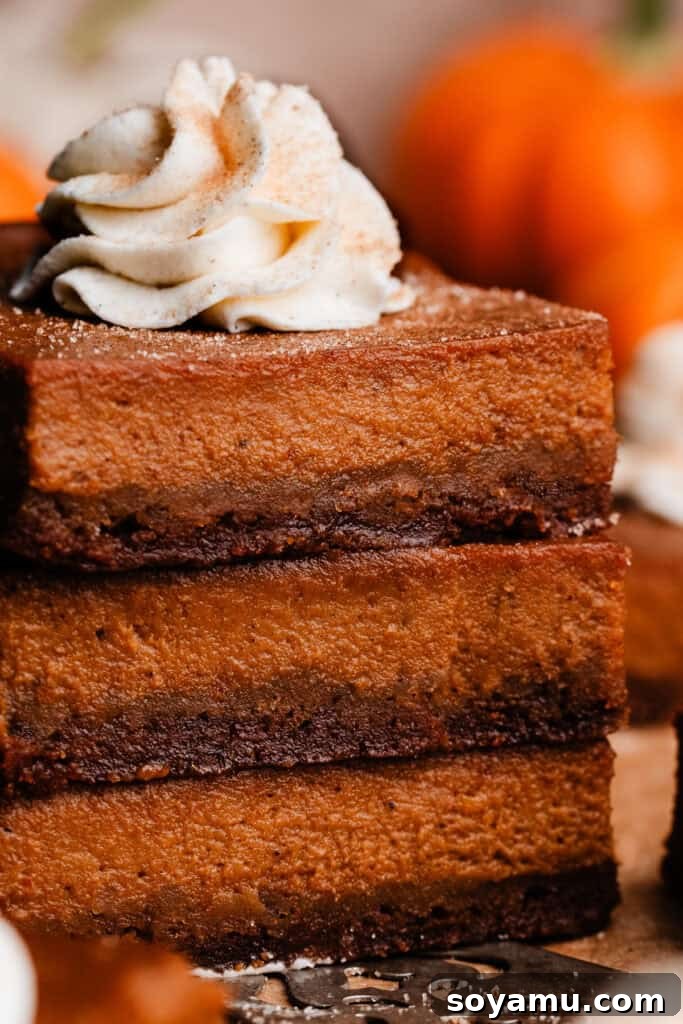 Perfectly Simple Pumpkin Pie Bars 10 A close-up of a stack of three pumpkin pie bars, with a generous swirl of whipped cream on top, showcasing the layers.
