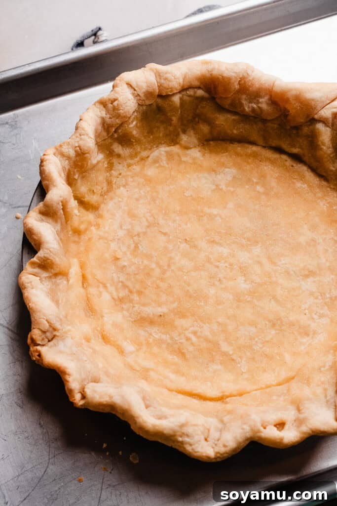 Autumn's Best Pumpkin Pie 5 The par-baked pie crust after removing parchment paper and pie weights, showing a firm and lightly golden base.