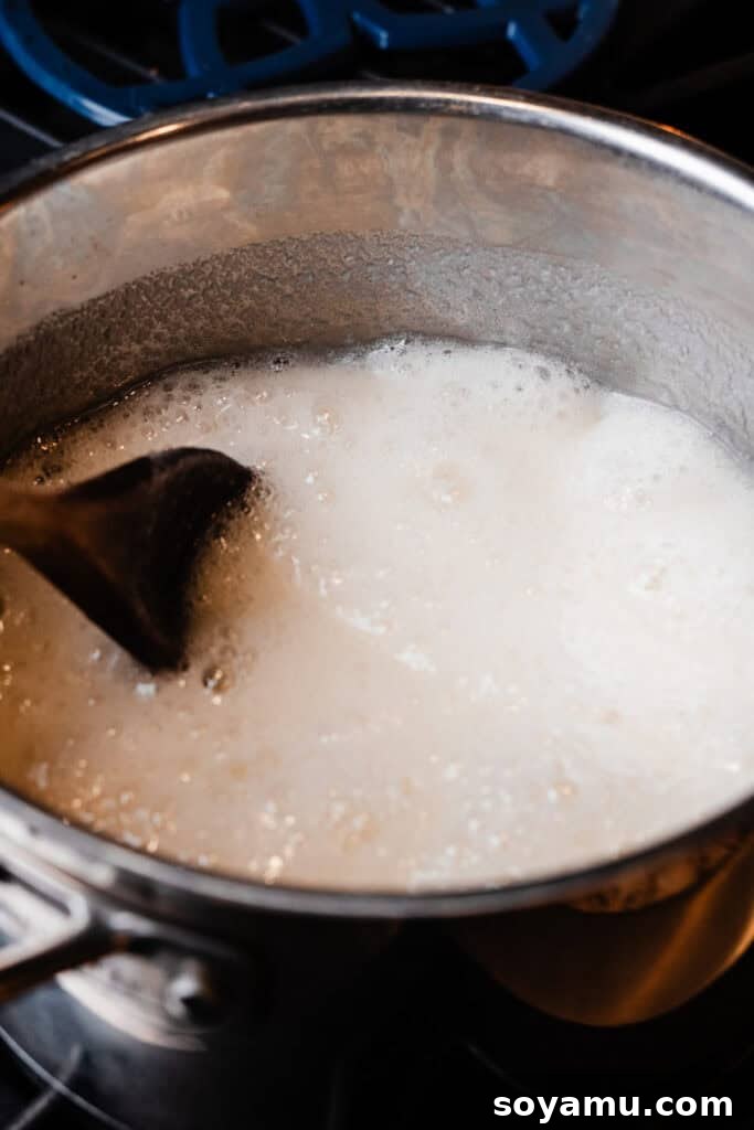 Sugar and whole milk actively boiling in a saucepan over medium-high heat, with a thermometer clipped to the side.