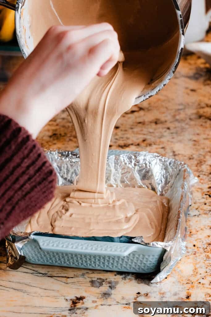 The smooth, warm peanut butter fudge mixture being carefully poured into the foil-lined 8x8-inch pan.