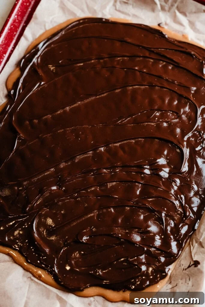 The smoothly spread layer of melted semi-sweet chocolate covering the toffee base, glistening and ready for nuts or other toppings to be added before setting.