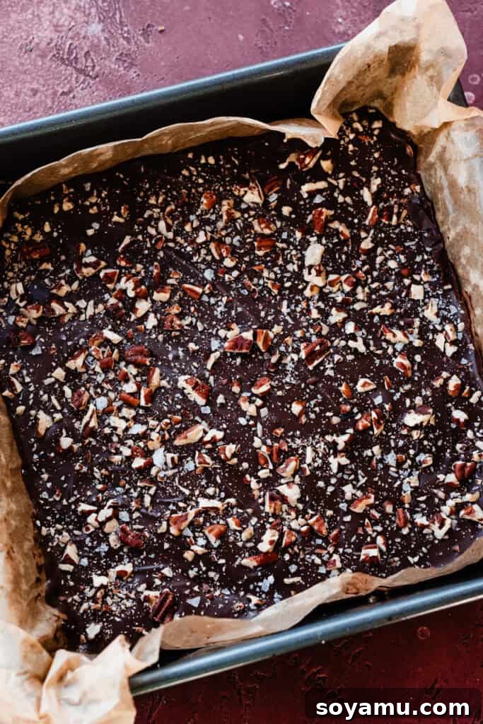 A perfectly cooled and set slab of homemade toffee, topped with chocolate and nuts, filling a 9x9 inch pan, ready to be broken into individual pieces.