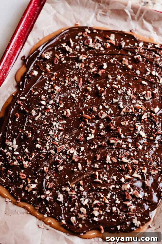 A large slab of finished homemade toffee, covered in chocolate and toasted pecans, spread thinly across a 9x13 inch cookie sheet, showcasing its golden hue and crisp texture.