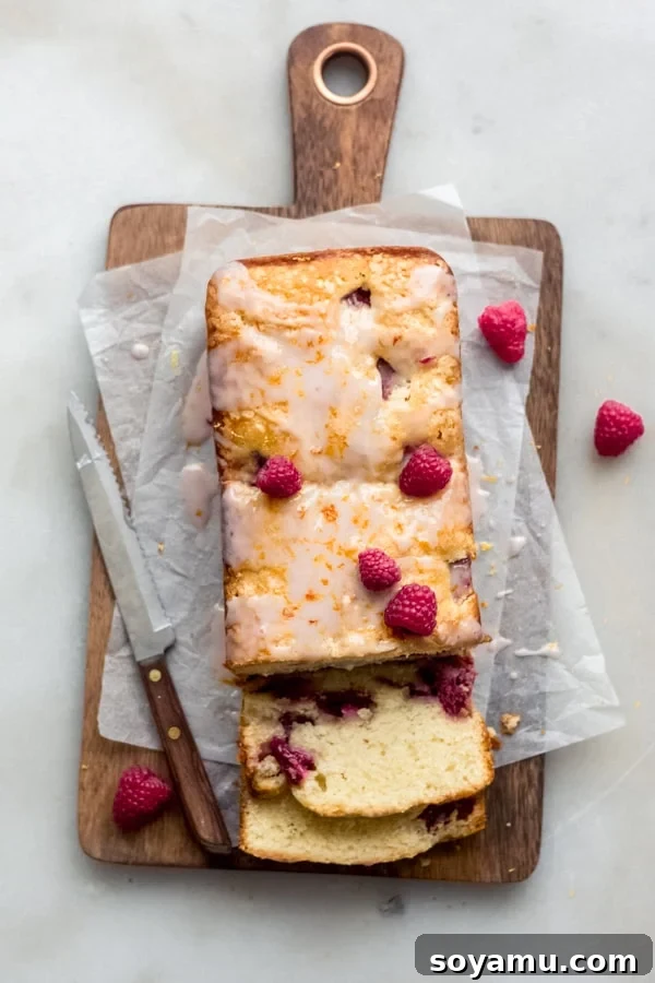 One Bowl Raspberry Lemon Bread - This quick bread is filled with spring flavor in the form of raspberries and lemon, it requires only one bowl and can be dressed up with a 2-ingredient glaze. It's flavorful, moist, and is begging to be baked immediately! #raspberrylemon #onebowlrecipe #quickbread #lemonbread #poundcake #lemoncake #springrecipes #springdesserts #dessertrecipes #bluebowlrecipes | bluebowlrecipes.com Vibrantly colored raspberry lemon bread on a wooden cutting board, showcasing its moist texture and delicate berries.
