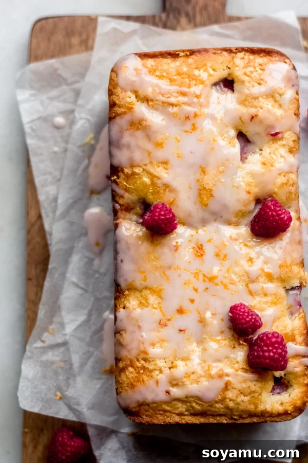 One Bowl Raspberry Lemon Bread - This quick bread is filled with spring flavor in the form of raspberries and lemon, it requires only one bowl and can be dressed up with a 2-ingredient glaze. It's flavorful, moist, and is begging to be baked immediately! #raspberrylemon #onebowlrecipe #quickbread #lemonbread #poundcake #lemoncake #springrecipes #springdesserts #dessertrecipes #bluebowlrecipes | bluebowlrecipes.com A beautiful top-down shot of raspberry lemon bread on a wooden cutting board, with slices ready to be enjoyed.