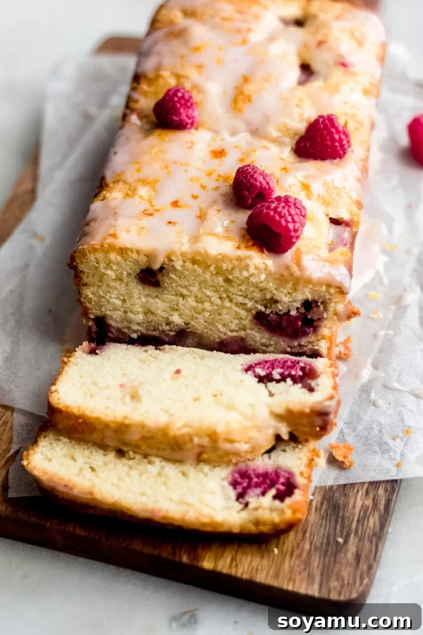 One Bowl Raspberry Lemon Bread - This quick bread is filled with spring flavor in the form of raspberries and lemon, it requires only one bowl and can be dressed up with a 2-ingredient glaze. It's flavorful, moist, and is begging to be baked immediately! #raspberrylemon #onebowlrecipe #quickbread #lemonbread #poundcake #lemoncake #springrecipes #springdesserts #dessertrecipes #bluebowlrecipes | bluebowlrecipes.com Sliced raspberry lemon bread on a rustic cutting board, highlighting the perfect golden crust and visible raspberries.