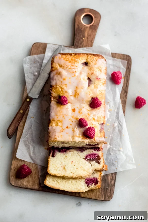 One Bowl Raspberry Lemon Bread - This quick bread is filled with spring flavor in the form of raspberries and lemon, it requires only one bowl and can be dressed up with a 2-ingredient glaze. It's flavorful, moist, and is begging to be baked immediately! #raspberrylemon #onebowlrecipe #quickbread #lemonbread #poundcake #lemoncake #springrecipes #springdesserts #dessertrecipes #bluebowlrecipes | bluebowlrecipes.com Beautifully glazed raspberry lemon bread with fresh raspberries and lemon zest on top, ready to serve.