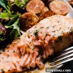 A close-up on a piece of flaky salmon on a plate, with a fork having removed a bite.