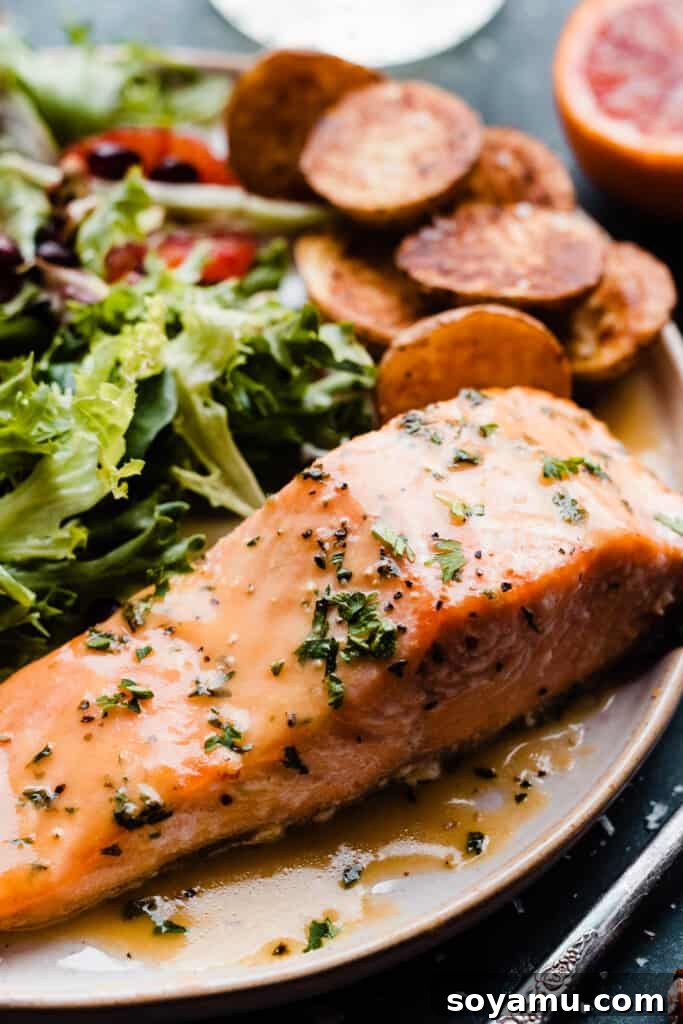 Sheet Pan Caramelized Maple Salmon with Crispy Potatoes 10 A close-up of a baked piece of maple glazed salmon on a plate, with a side salad & roast potatoes.