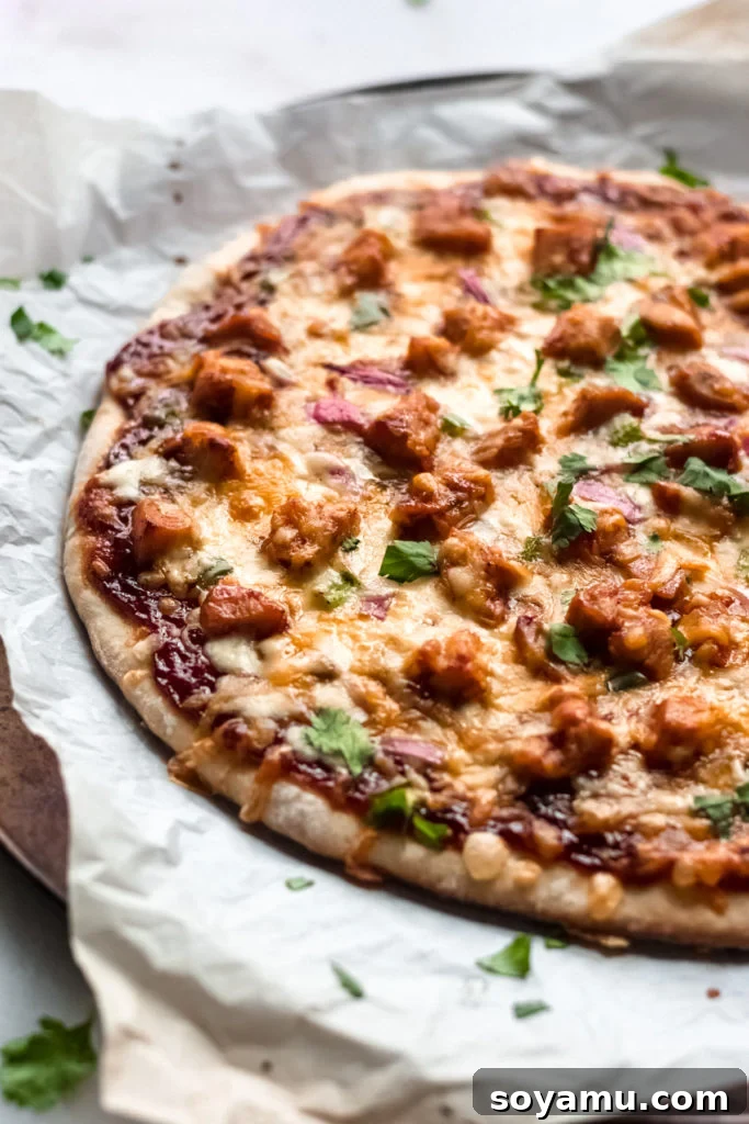 Our Favorite Barbecue Chicken Pizza - Pizza night just got even more delicious! An easy homemade crust is the base for this pizza made with chicken, barbecue sauce, mozzarella and colby jack cheese, green pepper, and red onion. This is what every weekend (and weeknight!) calls for! #barbecuechicken #chicken #pizza #barbecuechickenpizza #bbq #bbqchicken #homemadepizza #weeknightdinner #easydinner | bluebowlreicpes.com A close-up view of a golden-crusted barbecue chicken pizza, fresh from the oven.