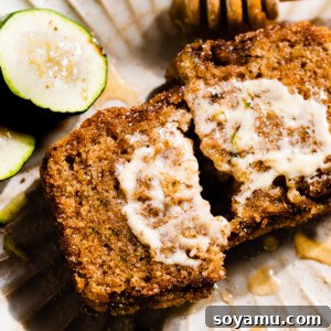 Two halves of a slice of zucchini bread on a plate, with a swoop of honey butter.